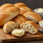 Freshly baked crusty chewy French bread rolls on a cutting board, highlighting their golden crust and soft texture.