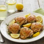 Rendered final view of savory lemon herb roasted chicken thighs, presented elegantly with herbs and lemons on a rustic table.