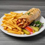 Completed Spicy Chicken Shawarma served on a rustic wooden table, garnished with parsley, alongside fries and pickles for a mouthwatering presentation.