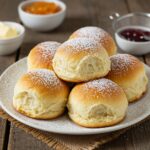 Delicious final presentation of breakfast rolls with powdered sugar, served with jam and butter, ideal for a morning treat.