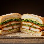 Final presentation of a Crispy Chicken Caesar Sandwich, cut in half to reveal the delicious layers of chicken, lettuce, and dressing, beautifully garnished.