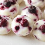 A close-up of vibrant blueberry swirl yogurt bites arranged on a white plate, showcasing their creamy texture with streaks of deep blue blueberry sauce, garnished with fresh blueberries and mint leaves, highlighting their colorful and appetizing appearance.