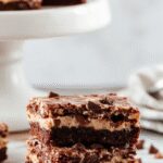 A close-up of a sliced chocolate mousse brownie showcasing its layered structure; a glossy, rich chocolate top layer contrasts with a lighter, creamy mousse inside, all displayed on a rustic wooden board with a soft focus background highlighting the indulgent treat.