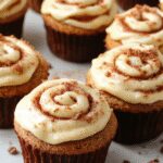 A tray of beautifully baked cinnamon roll cupcakes with golden-brown tops, topped with swirls of gooey cinnamon filling and a drizzle of icing. The cupcakes are arranged on a rustic wooden surface, with some icing dripping down the sides, showcasing their soft, fluffy texture and enticing swirl patterns.