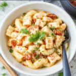 A vibrant creamy protein pasta bowl featuring al dente pasta coated in a smooth, rich sauce, topped with fresh herbs and grated cheese, presented in a stylish white bowl on a rustic wooden surface.