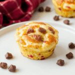 A close-up of golden-brown mini muffin-sized pancakes arranged on a white plate, with a drizzle of syrup and a dusting of powdered sugar, showcasing their fluffy texture and appealing size.