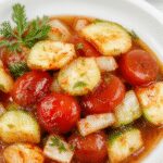 A clear glass jar filled with vibrant red cherry tomatoes, thinly sliced green onions, and crunchy cucumbers submerged in a tangy pickling brine, with visible herbs and spices around the jar, presented on a rustic wooden surface.