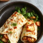 A vibrant sweet chili halloumi wrap sliced open to reveal golden grilled halloumi cheese, crisp fresh lettuce, and colorful bell peppers wrapped in a toasted tortilla with a drizzle of sweet chili sauce visible on the filling.