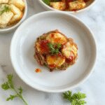 A steaming plate of hearty comfort food featuring a generous serving of golden-brown, crispy fried chicken garnished with fresh herbs, accompanied by creamy mashed potatoes and vibrant steamed vegetables, all presented on a rustic ceramic plate with a rustic wooden table background.