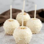 A close-up of glossy white candy apples decorated with edible glitter, arranged on a elegant platter with a festive winter backdrop. The apples are smooth, shiny, and perfectly round, with some topped with sparkles, presenting a luxurious and festive appearance.