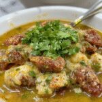 A vibrant bowl of Beef Chile Verde showcasing tender chunks of beef submerged in a bright green sauce, garnished with fresh cilantro and served alongside warm tortillas. The dish's glossy, thick sauce and succulent meat are visually appealing against a rustic wooden table backdrop.
