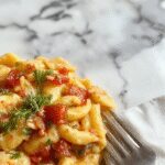 A vibrant plate of cooked orzo pasta garnished with fresh herbs and cherry tomatoes, presented on a rustic wooden table with a fork twirling the pasta, showcasing its tender texture and colorful ingredients.