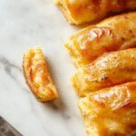 A close-up of freshly baked homemade breakfast rolls arranged on a rustic wooden platter, golden-brown crust with a soft, airy interior visible at the cut edge, steam rising gently, with a few rolls stacked and some slightly pulled apart, showcasing their fluffy texture and inviting appearance.