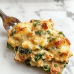 A creamy chicken and spinach casserole in a rustic oval dish, topped with melted cheese and fresh basil leaves. The dish showcases golden-brown edges, vibrant green spinach, tender chicken chunks, and a smooth, cheesy sauce, presented on a wooden table with a fork and a side of crusty bread.