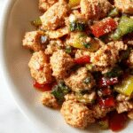 A vibrant stir-fry dish featuring ground turkey cooked with colorful bell peppers in red, yellow, and green, garnished with chopped green onions on a white plate, with a rustic wooden background and chopsticks on the side.