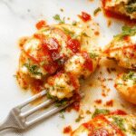 A close-up of creamy spinach and ricotta stuffed pasta shells arranged on a white ceramic plate. The shells are golden with green spinach filling visible, garnished with a sprinkle of grated cheese and fresh herbs, with a vibrant green spinach leaves backdrop.