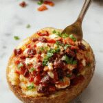 A vibrant loaded potato taco bowl featuring crispy roasted potato chunks topped with freshly diced tomatoes, shredded lettuce, melted cheese, and tangy sour cream, all arranged in a rustic bowl garnished with chopped cilantro and lime wedges, highlighting a colorful and inviting presentation.