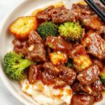 A vibrant stir-fry featuring tender ground beef glazed with a glossy honey garlic sauce, nestled among bright green broccoli florets and garnished with sesame seeds on a white plate. The dish has a rich, caramelized appearance with a balanced mix of textures, showcased in a clean, modern setting.