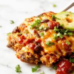 A savory slow cooker taco casserole displayed in a rustic ceramic dish, topped with melted cheese, fresh chopped cilantro, and sliced jalapeños, with colorful layers of seasoned ground beef, beans, and crunchy taco shell pieces visible.