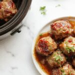 A rustic white platter showcasing tender Salisbury steak meatballs glazed with rich gravy, garnished with fresh parsley, surrounded by roasted vegetables on a warm wooden table.
