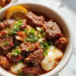 A vibrant beef and pepper rice bowl garnished with fresh herbs, featuring glossy slices of seasoned beef, colorful bell peppers, and fluffy rice, arranged elegantly in a white bowl on a rustic wooden surface.