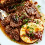 A rustic, hearty Italian pot roast served on a deep white plate. The beef is tender, shredded slightly, with a rich brown sauce surrounding it. Garnished with fresh herbs, golden roasted vegetables, and accompanied by creamy, textured Gorgonzola polenta. The presentation emphasizes the comforting, homestyle culinary tradition with a warm, inviting atmosphere.