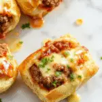 A close-up of golden-brown Philly Cheesesteak Rolls sliced open to reveal tender steak, melted provolone cheese, and sautéed peppers inside a crispy, flaky roll with a rustic wooden background.