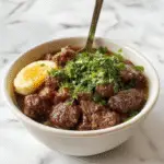 A vibrant Korean ground beef bowl featuring a perfectly seasoned, caramelized ground beef topping arranged over a bed of fluffy white rice. The dish is garnished with finely chopped green onions, sesame seeds, and thin slices of red chili for color contrast. The bowl sits on a rustic wooden table with a side of fresh vegetables and a small dish of soy sauce, highlighting the dish's savory and spicy elements. The image captures the appetizing texture and rich colors of the ingredients, creating an inviting, high-quality food presentation.