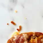 A beautifully sliced pumpkin bread loaf with a golden-brown crust sits on a rustic wooden table. The bread reveals a soft, moist interior speckled with spices, and a few slices are fanned out to showcase its tender crumb. The background includes a cozy fall-themed setting with pumpkins, cinnamon sticks, and a hint of autumn leaves, emphasizing warmth and seasonal flavor.