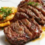 A plated Salisbury steak served topped with rich mushroom-onion gravy, garnished with fresh herbs. The steak has a golden-brown crust, complemented by caramelized onions and sliced mushrooms in a glossy sauce, presented on a rustic white plate with a sprig of parsley for garnish.