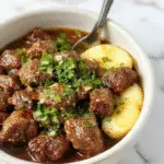 A vibrant bowl filled with seasoned ground beef, topped with fresh chopped herbs, served on a rustic wooden table with ingredients like tomatoes and greens visible around.