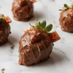 A festive plate featuring two chocolate-covered strawberries shaped like turkeys, with a drizzle of dark chocolate over bright red strawberries. The turkeys are decorated with tiny candy eyes and candy corn as beak and feathers, set on a decorative Thanksgiving-themed table with autumn leaves and small gourds in the background.