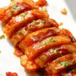 A close-up of several roasted carrots wrapped in crispy bacon, glazed with a shiny maple syrup, arranged on a rustic wooden platter. The caramelized edges of the bacon are visible, and the carrots are tender with a golden hue, garnished with a sprinkle of fresh herbs.