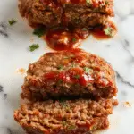 A close-up of several savory mini meatloaves baked to a golden brown, arranged neatly on a white plate. Each mini meatloaf is topped with a thin glaze and garnished with fresh herbs, displaying a moist, tender texture with crispy edges. The background features a rustic wooden table and a side of colorful vegetables, highlighting the comforting and homey appeal.