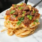 A bowl of Mongolian Ground Beef Noodles showcasing tender ground beef glazed with savory sauce, vibrant green scallions, and tender noodles, garnished with sesame seeds, all plated in a rustic ceramic bowl.
