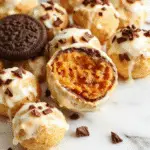 Close-up of pumpkin-shaped Oreo balls coated in orange candy melts with black icing accents, arranged on a white platter with festive Halloween decorations in the background, highlighting their smooth texture and playful design.